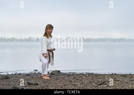 Young Woman in Kimono practicing karate, Japanese martial arts on river coast. Early foggy morning Stock Photo