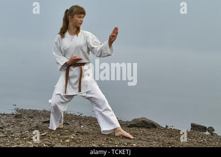 Young Woman in Kimono practicing karate, Japanese martial arts on river coast. Early foggy morning Stock Photo