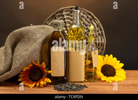oil in bottles, sunflowers and seeds, on wooden table on brown background Stock Photo