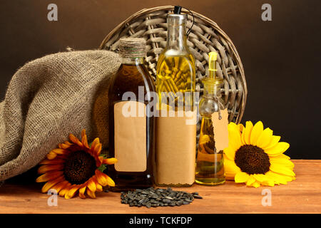 oil in bottles, sunflowers and seeds, on wooden table on brown background Stock Photo