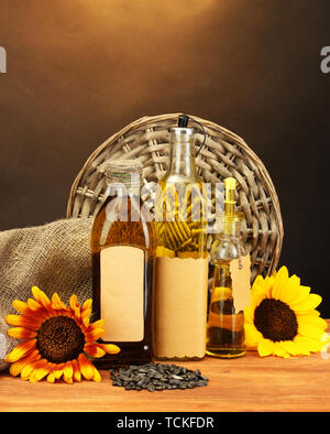 oil in bottles, sunflowers and seeds, on wooden table on brown background Stock Photo