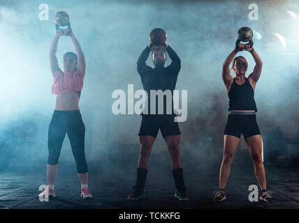 Group of athletes swinging a kettle bell over their head in crossfit gym Stock Photo