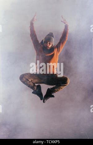 Male breakdancer jumps off high in the air while performing a cool dance move, a lot of smoke in the background. Stock Photo