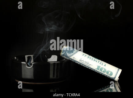 smoking cigar of the 100 dollar bill and an ashtray isolated on black background Stock Photo