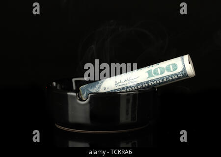 smoking cigar of the 100 dollar bill and an ashtray isolated on black background Stock Photo