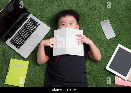 seven years old child reading a book lying on the grass Stock Photo