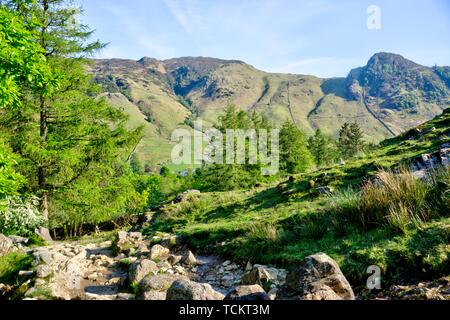 View of Langdale in English Lake District in United Kingdom in evening sunshine with dry stone wall and rocky path in foreground