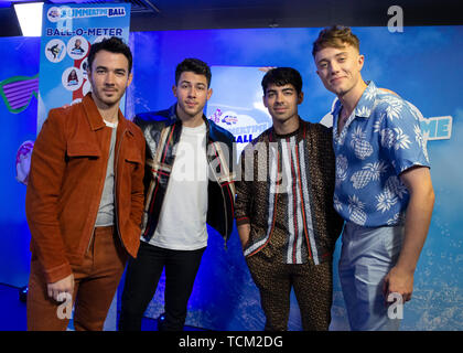 (left to right) Kevin Jonas, Nick Jonas and Joe Jonas of the Jonas Brothers join Capital FM presenter Roman Kemp in the on air studio during Capital's Summertime Ball. The world's biggest stars perform live for 80,000 Capital listeners at Wembley Stadium at the UK's biggest summer party. Stock Photo