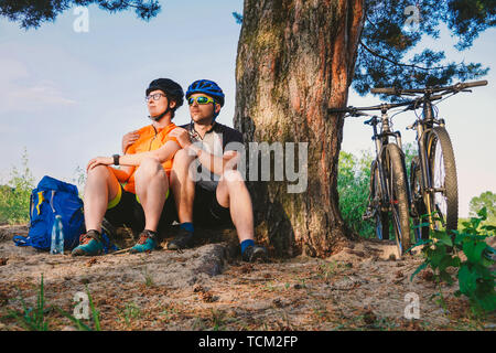 Happy couple with mountain bike sit embracing leisure nature outdoors. happy couple, lead an active lifestyle, stopped in woods near tree take a break Stock Photo