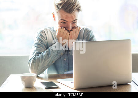 Scared or nervous! Portrait of emotional nervous young businessman in blue shirt are sitting in cafe working online and nail biting himself cause made Stock Photo