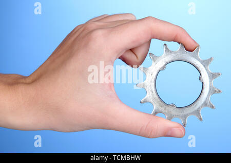 Man holding metallic cogwheel in his hand on blue background Stock Photo