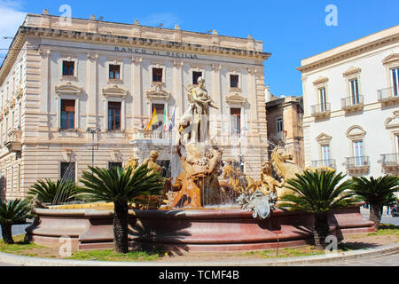 Syracuse, Sicily, Italy - Apr 10th 2019: Beautiful Fountain of Diana on the Archimedes Square in famous Ortigia Island. Building of a Sicilian bank in the background. Sunny day, blue sky. Stock Photo
