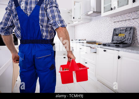 Rear View Of A Repairman In Uniform Holding Tool Box Installing Kitchen Induction Ceramic Hob Stock Photo