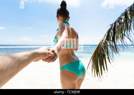 Young Woman Holding Hand Of Her Boyfriend Going Toward The Sea At Beach Stock Photo