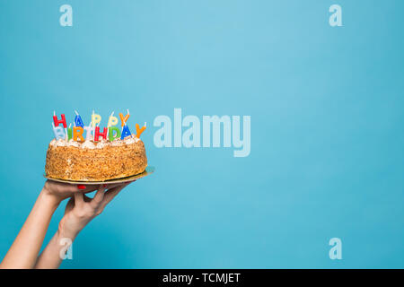 Hands holding a birthday cake with candles and the inscription birthday on a blue background. Copy Space Stock Photo