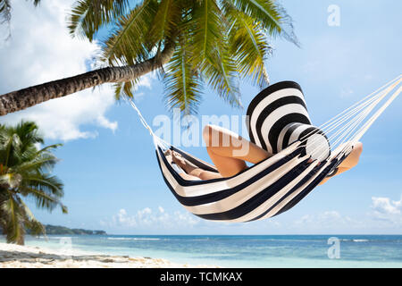 Close-up Of A Woman Relaxing On Striped Hammock Tied On Palm Tree At Idyllic Beach Stock Photo