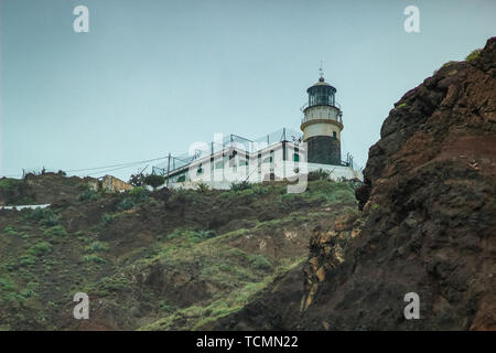 Steep high lava rock cliffs on on the east of Tenerife. Sea lighthouse, natural sky background. Stock Photo