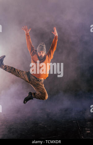 Male breakdancer jumps off high in the air while performing a cool dance move, a lot of smoke in the background. Stock Photo