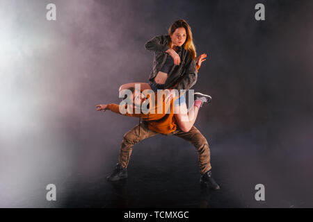 Strong male dancer and an elegant female dancer perform an exotic and unique dance moves in front of a black background while wearing urban clothes. Stock Photo