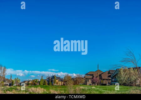Homes on a vast field against vibrant blue sky with puffy clouds on a sunny day Stock Photo