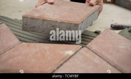 Worker lay tiles on the sidewalk. Laying concrete paving slabs in house courtyard driveway patio. Professional workers bricklayers are installing new Stock Photo