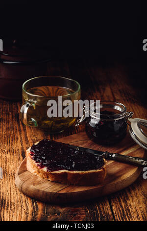 Toast with berry jam on cutting board and cup of green tea in rustic setting Stock Photo