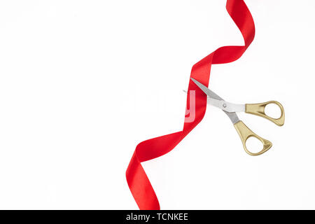 Grand opening. Top view of gold scissors cutting red silk ribbon on white background Stock Photo