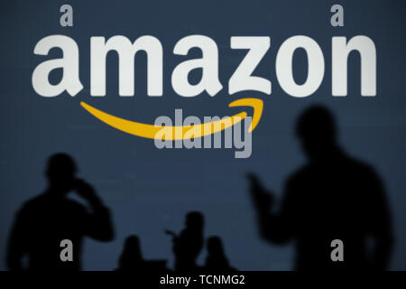 The Amazon logo is seen on an LED screen in the background while a silhouetted person uses a smartphone in the foreground (Editorial use only) Stock Photo