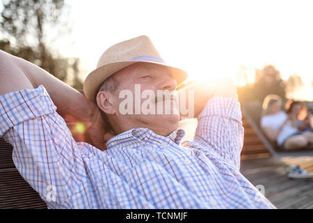 Old hispanic man sits on bench, smiling, enjoying summer sunny day. Stock Photo