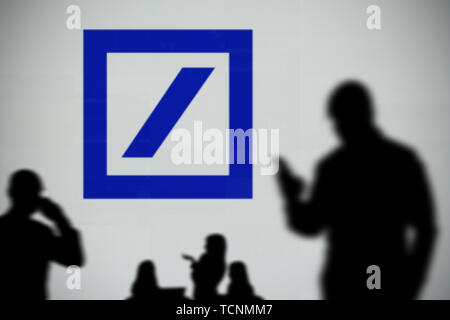 The Deutsche Bank logo is seen on an LED screen in the background while a silhouetted person uses a smartphone in the foreground (Editorial use only) Stock Photo