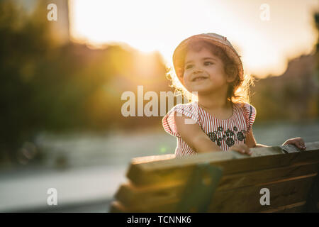 Portrait of a cute beautiful and happy girl standing on bench in the park. Stock Photo