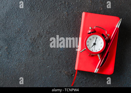 Alarm clock, notepad and pen on dark background. Concept time management or education. Copy space. Stock Photo