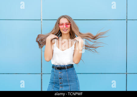 Portrait of beauty fashion smiling woman with flying hairstyle, in pink neon sunglasses on blue background. Casual Stock Photo