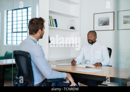 African American office manager going over notes and paperwork with a colleague while sitting at his desk Stock Photo