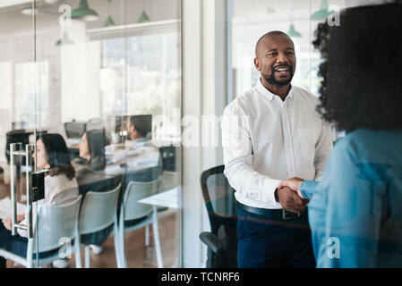 Smiling African American manager shaking hands with a new employee after an interview while standing together in his office Stock Photo