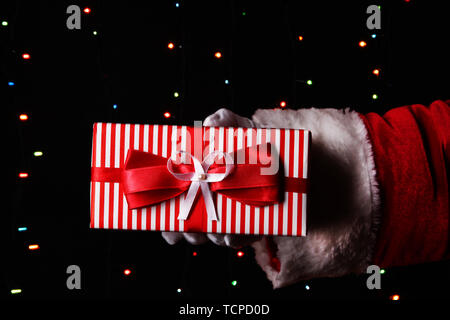 Santa Claus hand holding gift box on bright background Stock Photo
