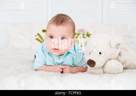 photo of little boy is lying on the bed next to a teddy bear Stock Photo