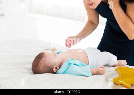 Photo of Mom put the baby on the bed and changes his clothes Stock Photo