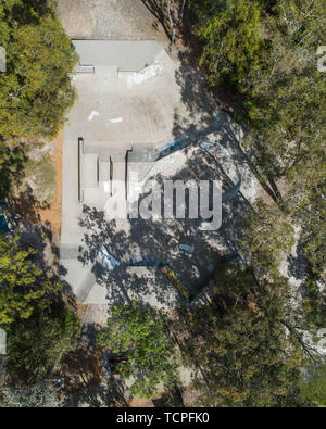 Skate park view fron the sky taken from a drone in the middle of a park with trees in Australia. Beautiful aerial view of fun ride, freestyle and tric Stock Photo