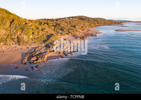 Beautiful aerial view of a beach escape with nice beach, rocks and warm gentle waves. Beach strand with white sand and lite sunset glow Stock Photo