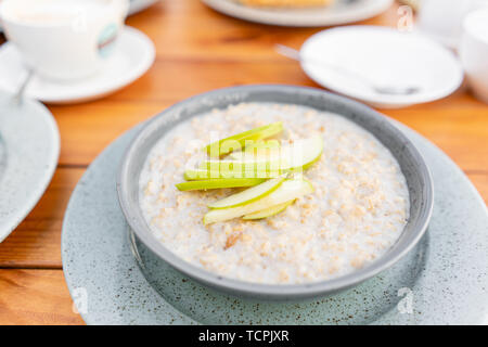 Breakfast and coffee in the summer cafe. Fresh oatmeal porridge with apples, honey, nuts and cinnamon close up for healthy breakfast Stock Photo
