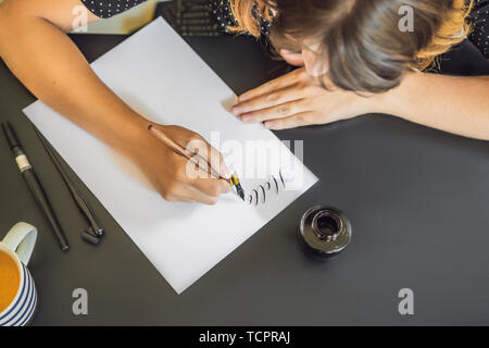 Calligrapher Young Woman writes phrase on white paper. Inscribing ornamental decorated letters. Calligraphy, graphic design, lettering, handwriting Stock Photo