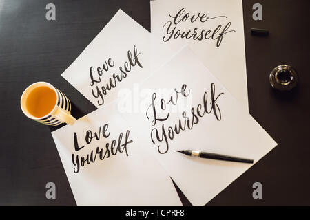 Love yourself. Calligrapher Young Woman writes phrase on white paper. Inscribing ornamental decorated letters. Calligraphy, graphic design, lettering Stock Photo