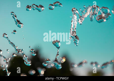 Water droplets frozen in the air with splashes and chain bubbles on a green and turquoise isolated background in nature. Clear and transparent liquid  Stock Photo
