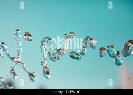 Water droplets frozen in the air with splashes and chain bubbles on a green and turquoise isolated background in nature. Clear and transparent liquid  Stock Photo