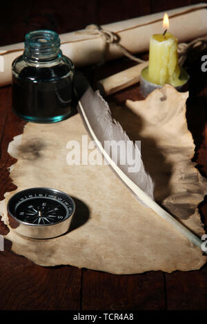 Old paper with ink pen near lighting candle on wooden table Stock Photo
