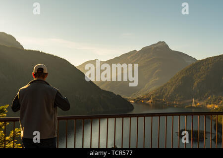 A man with a hat and vest watches the sunset over Diablo Lake from Vista Point in North Cascades National Park. Stock Photo