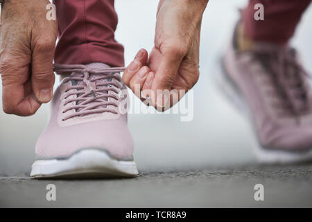 Hands of mature sportswoman tying shoelace of right cross-shoe while getting ready for jogging or working out on stadium Stock Photo