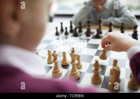 Hand of girl in purple sweater making first chess move in chess game against boy in white shirt Stock Photo