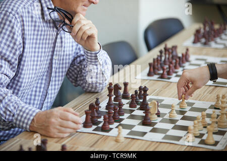 Men in checked shirt holding glasses in left hand playing chess with another man with black bracelet on right hand Stock Photo